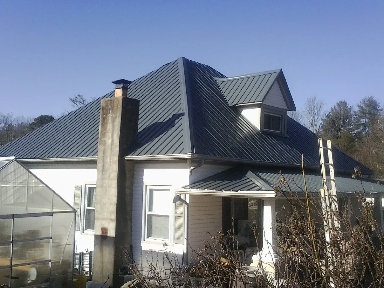Dark blue standing seam metal roof on a white farmhouse with dormer — Slate & Tile Roof Repair by Roofing Brothers in Logandale
