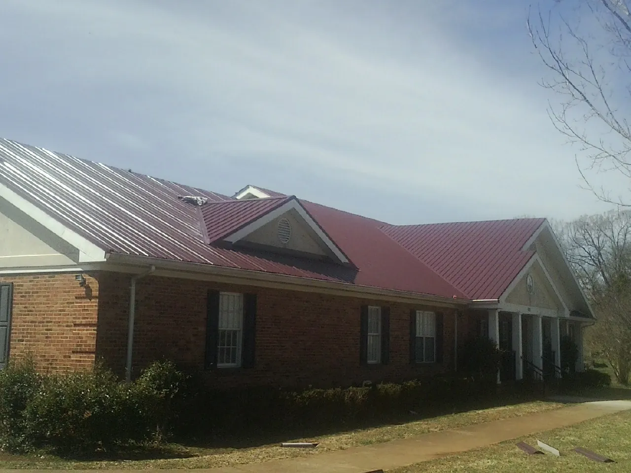Red metal roof with gabled entries on a long brick building, from a Hail Damage Roof Repair job in Logandale