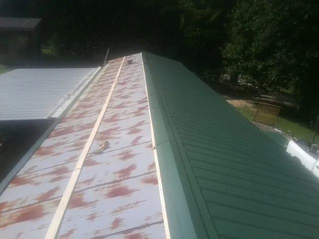 Old rusted panels beside newly installed green metal roofing — Wind Damage Roof Repair by Roofing Brothers in Logandale