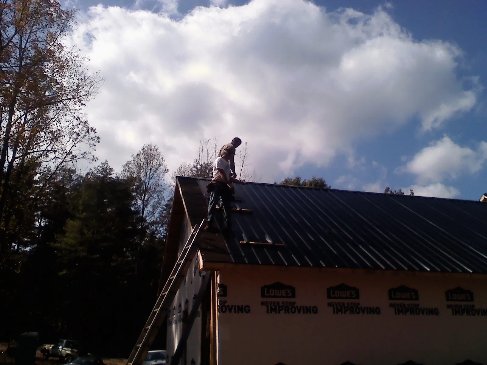 Roofer fastening dark metal panels high against a cloudy sky, from a Roof Inspection job in Logandale